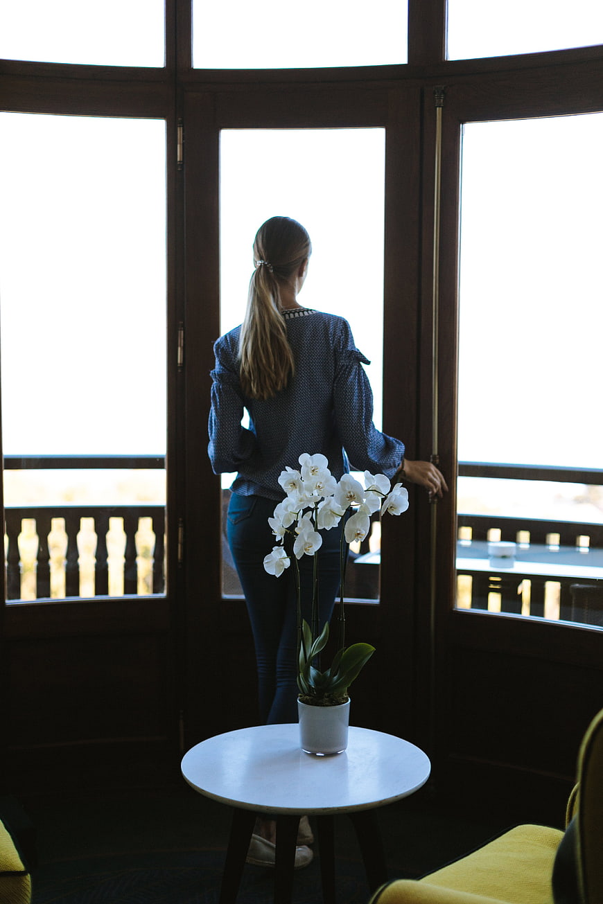Woman looking out window with white orchid on table