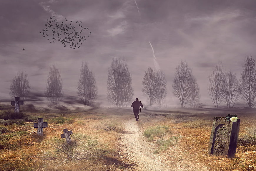 Lonely man walking through misty graveyard with tombstones