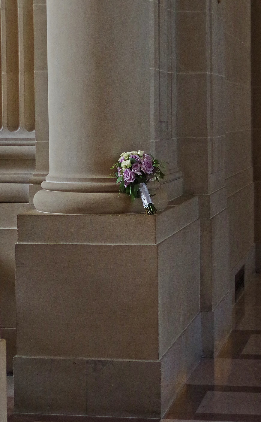 Purple and white wedding bouquet resting on stone pillar