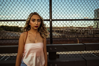 Stylish Woman in Pink Top Against Chain Link Fence