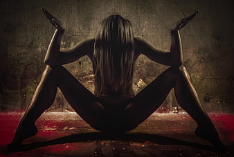 Silhouette of woman performing acrobatic yoga pose in dark studio