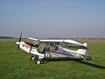 White ultralight aircraft parked on grassy airfield