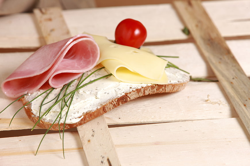 Open-faced sandwich with ham, cheese, and chives on wooden board