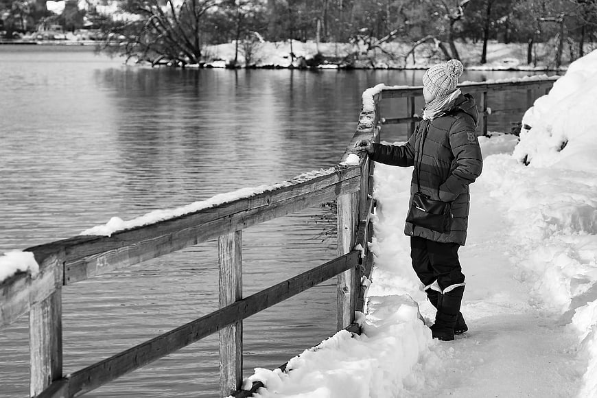 Man in winter coat standing by snowy river railing