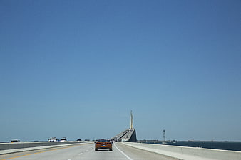 Orange sports car driving on bridge over ocean