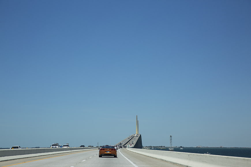 Orange sports car driving on bridge over ocean