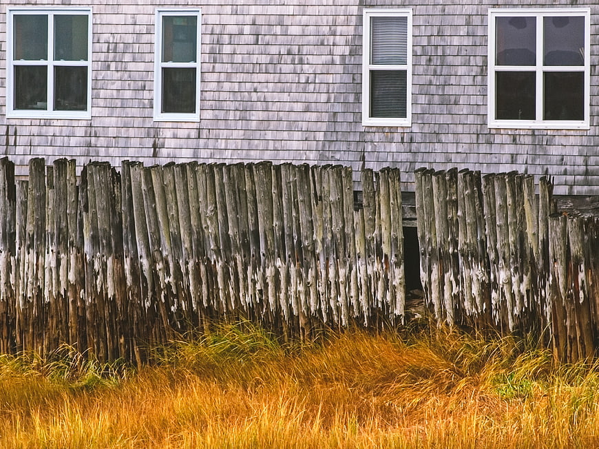 Weathered wooden fence in front of rustic shingled house