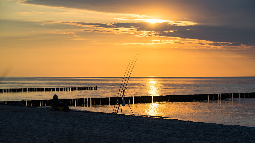 Silhouette of Fisherman and Rods on Baltic Sea Beach at Sunset