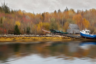 Blue fishing boat docked at rustic autumn harbor with colorful forest