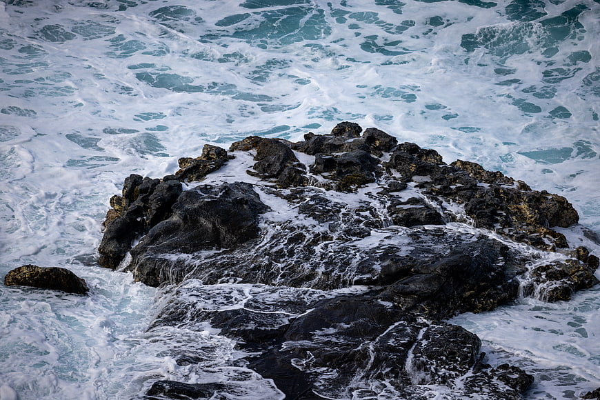 Aerial View of Turbulent Ocean Waves Crashing on Dark Rocks