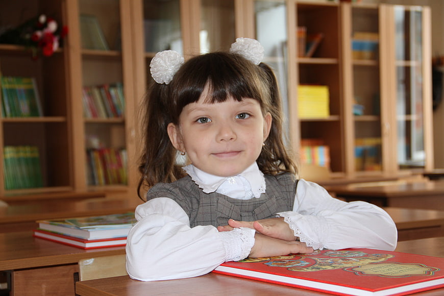 Cute schoolgirl with pigtails sitting at desk with books