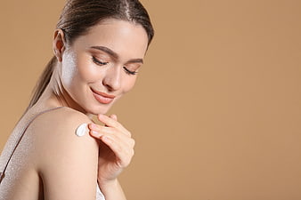 Woman applying moisturizer cream on shoulder skin