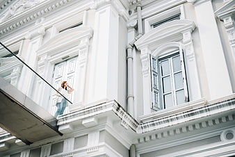 Woman standing on balcony of white classical architecture