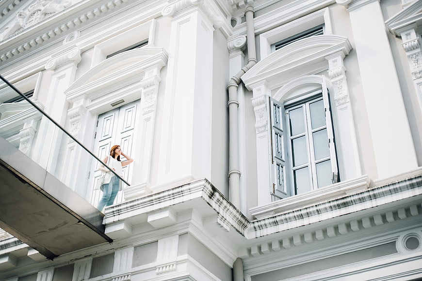Woman standing on balcony of white classical architecture