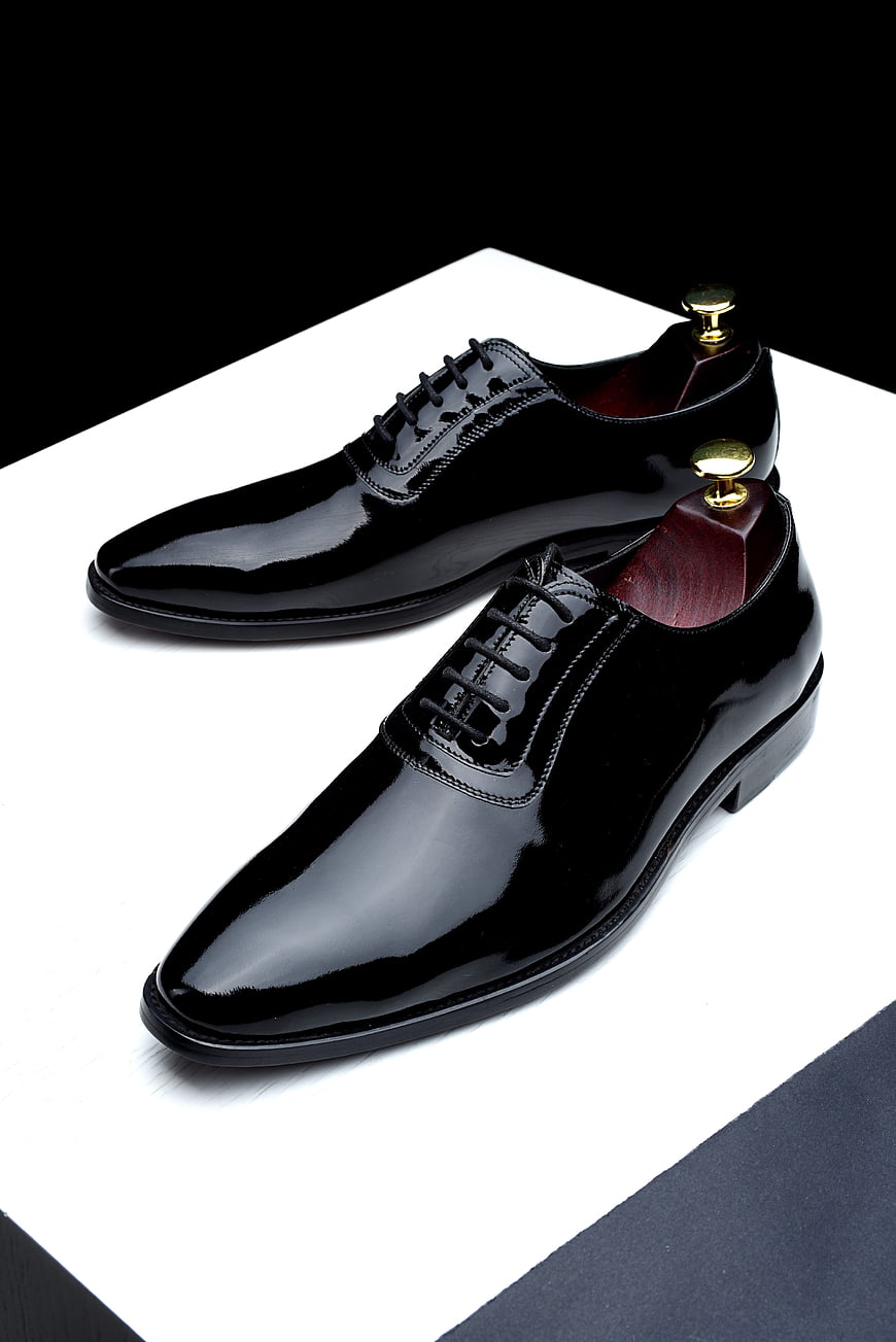 Black Patent Leather Oxford Shoes With Shoe Trees On White Surface