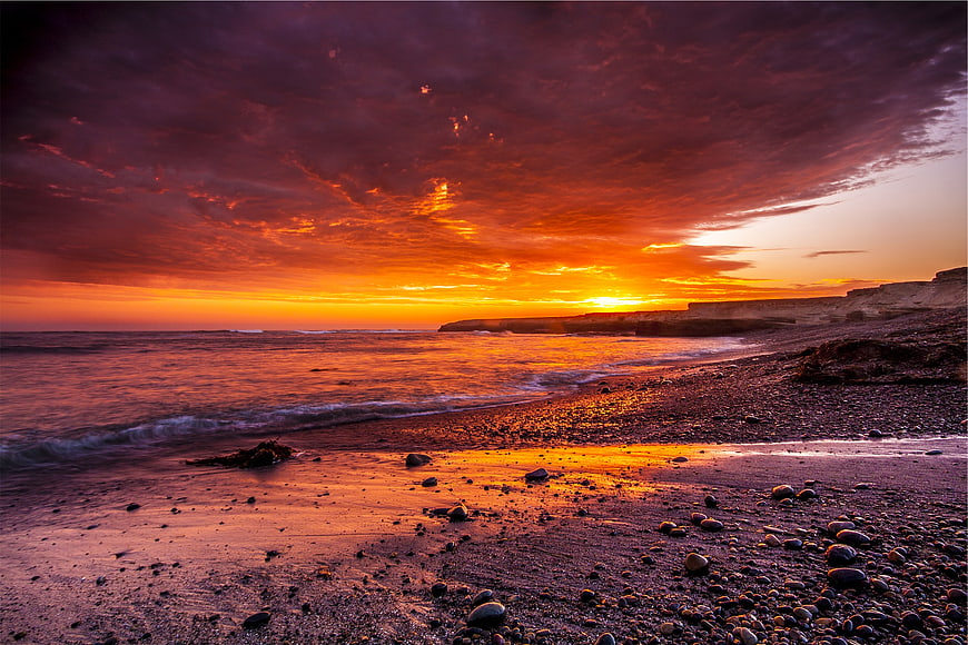 Dramatic fiery sunset over rocky beach with cliffs