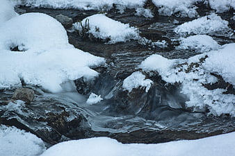 Frozen winter stream flowing through snow-covered rocks
