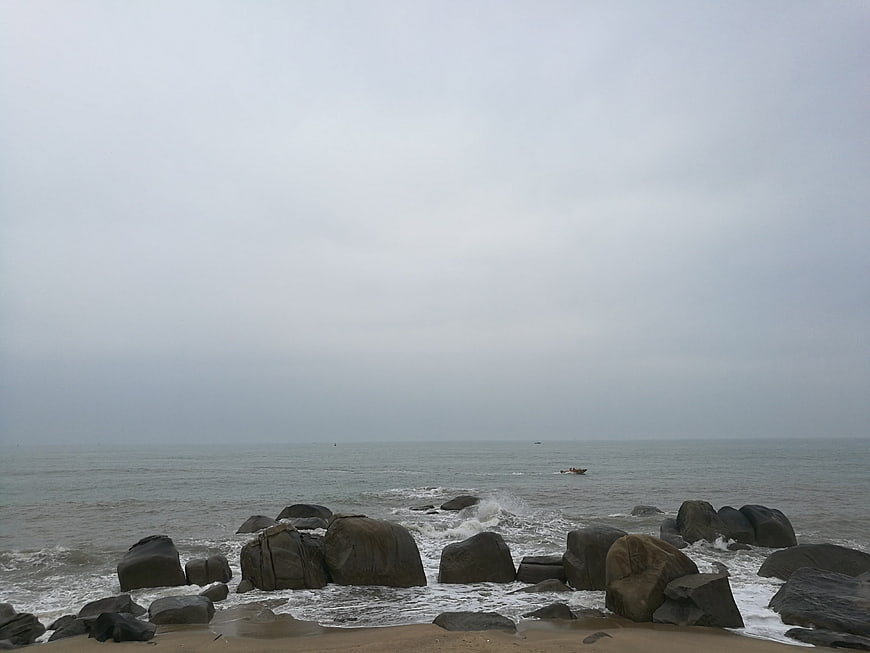 Overcast rocky beach with gray sea and distant boat