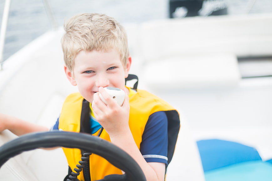 Young Boy Steering Boat with Yellow Life Jacket