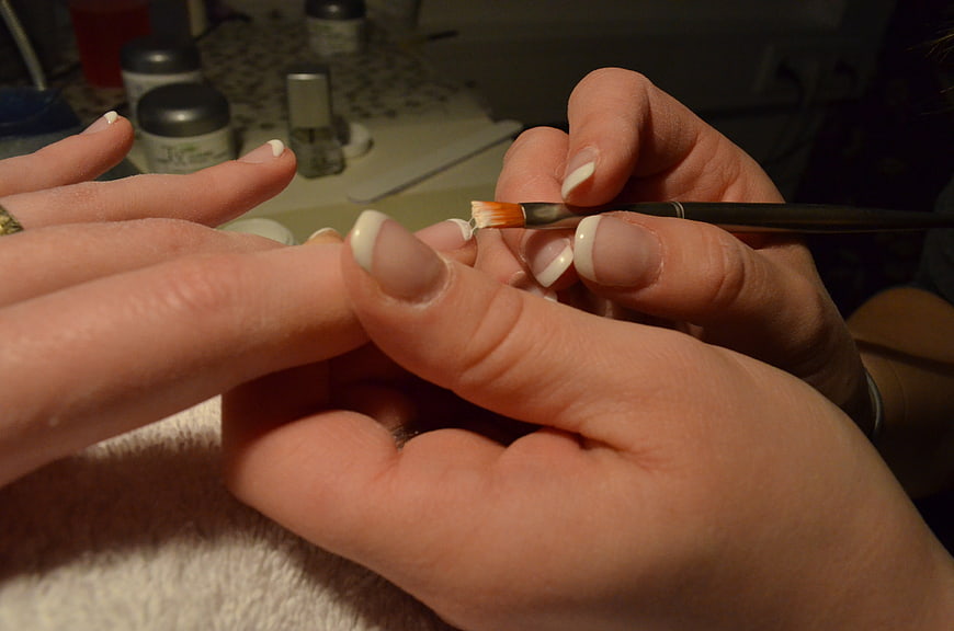 Close-up of hands applying French manicure nail design with brush