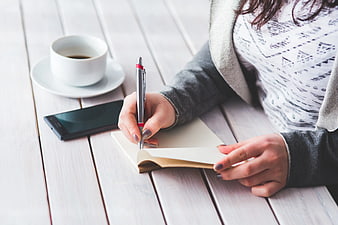 Woman writing in notebook with coffee and smartphone