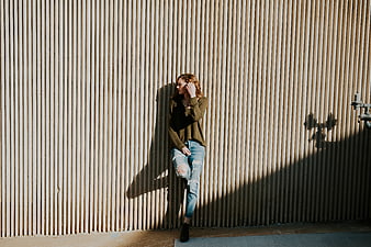 Woman in ripped jeans leaning against corrugated metal wall