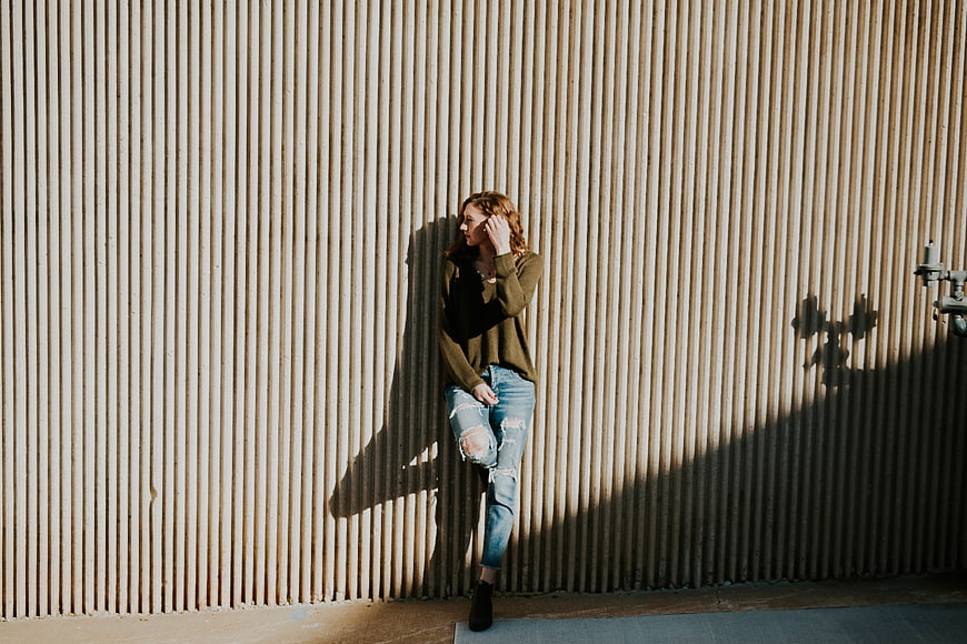 Woman in ripped jeans leaning against corrugated metal wall