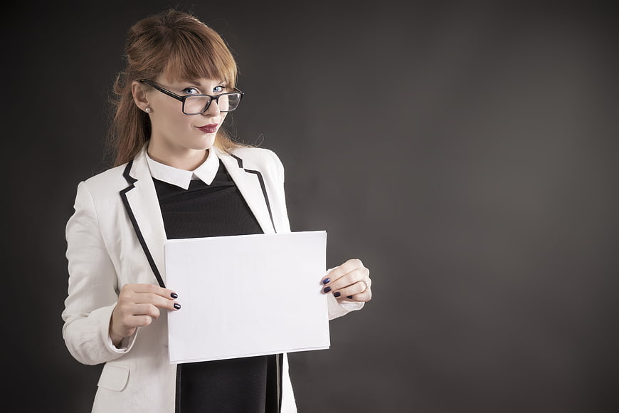 Businesswoman in white blazer holding blank white paper against dark background