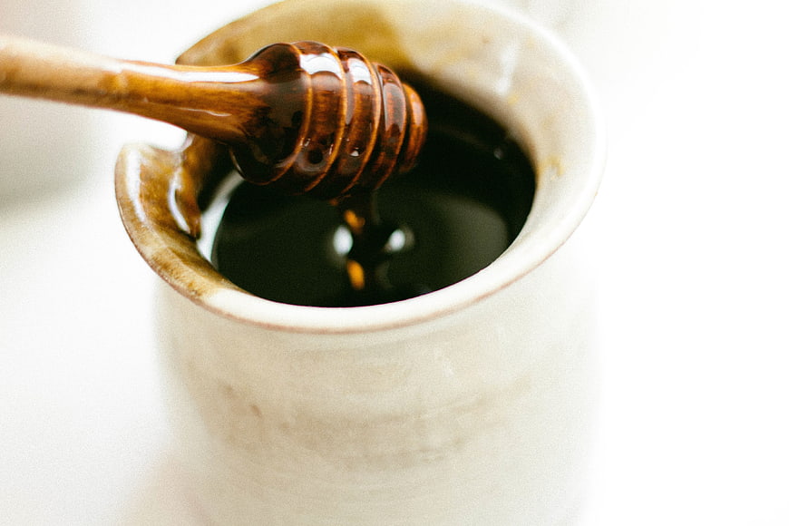 Close-up of wooden honey dipper in ceramic jar