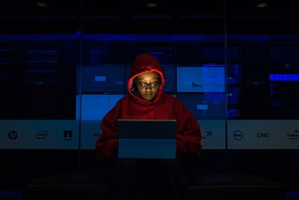 Woman in red hoodie coding on laptop in server room