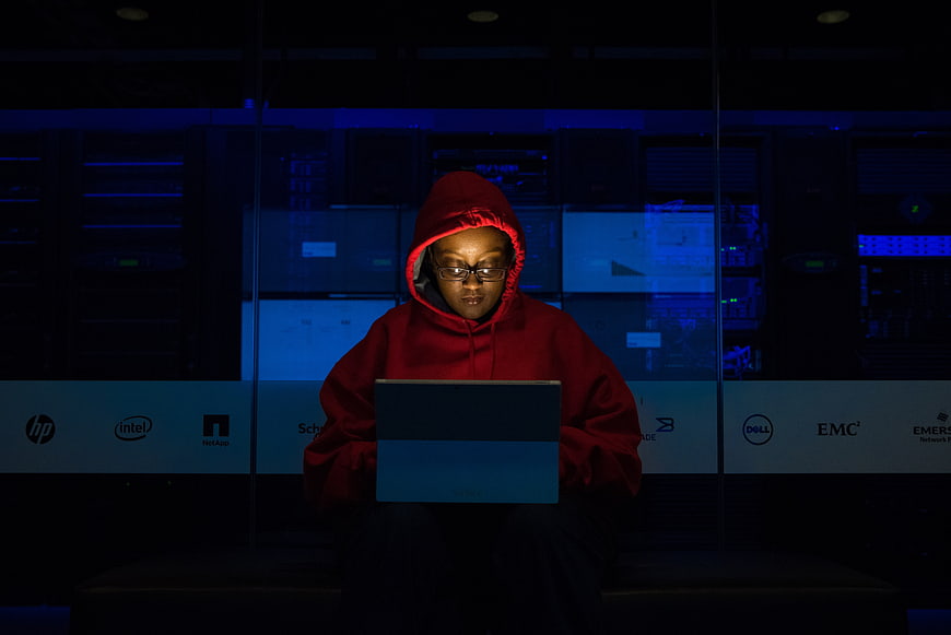 Woman in red hoodie coding on laptop in server room