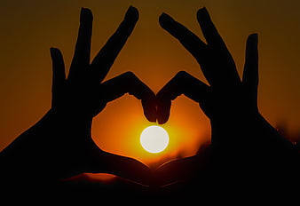 Silhouette of hands forming a heart shape around a bright sunset sun