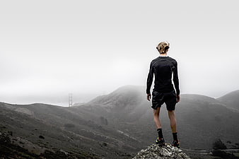 Man standing on rocky peak overlooking foggy Golden Gate Bridge