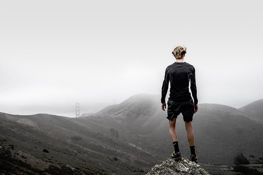 Man standing on rocky peak overlooking foggy Golden Gate Bridge