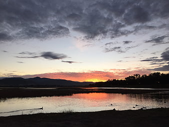 Dramatic sunset over lake with ducks and mountains