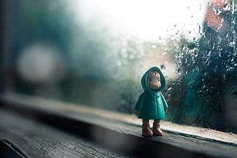 Small toy figure in raincoat standing by rainy window