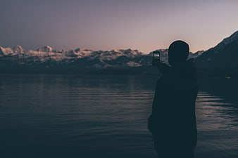 Silhouette of person taking photo of snowy mountains at dusk