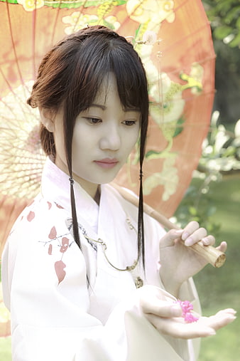 Young Asian woman in traditional white hanfu holding a pink flower and orange paper umbrella