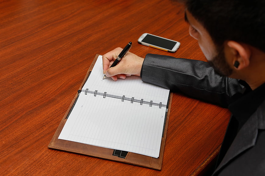 Businessman Writing in Notebook on Wooden Desk