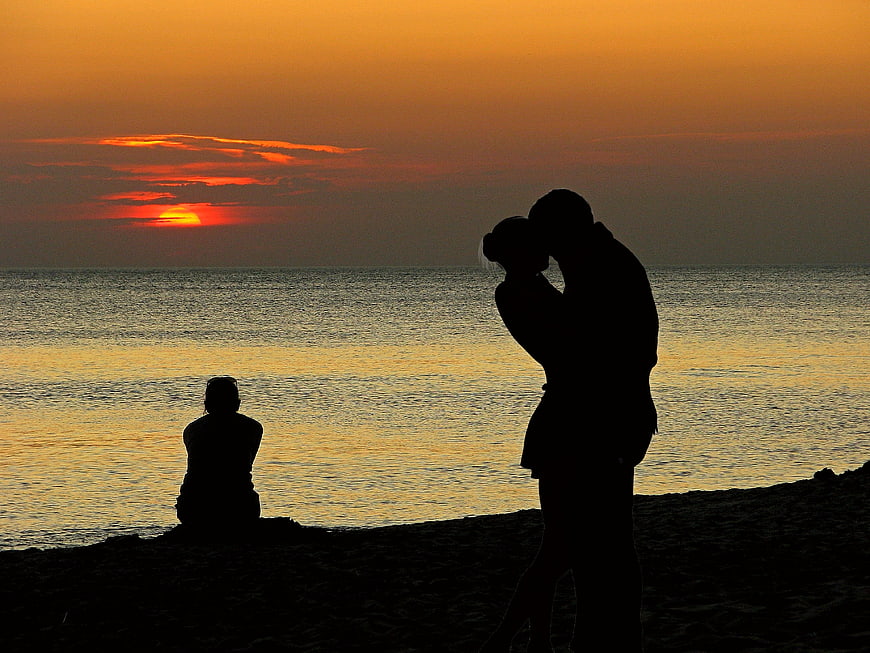 Silhouette of couple kissing at sunset on beach with observer