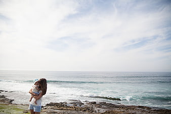 Mother holding baby on rocky beach looking at ocean