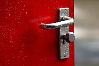 Close-up of a wet red door with a silver handle and raindrops