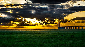Dramatic sunset over green field with bridge silhouette