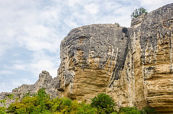 Dramatic limestone cliff face with green vegetation and cloudy sky