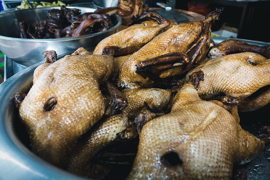 Glossy roasted ducks piled in a metal bowl