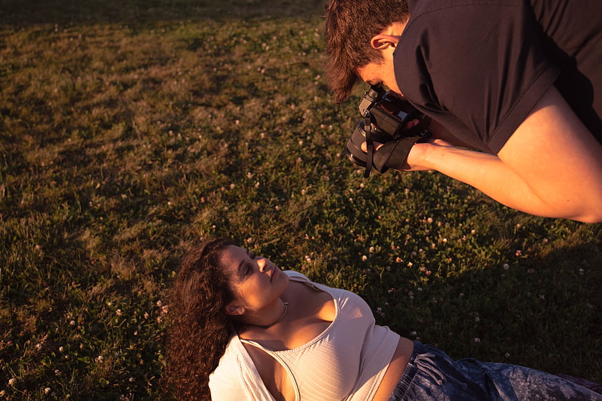 Photographer taking portrait of woman lying in grass at sunset