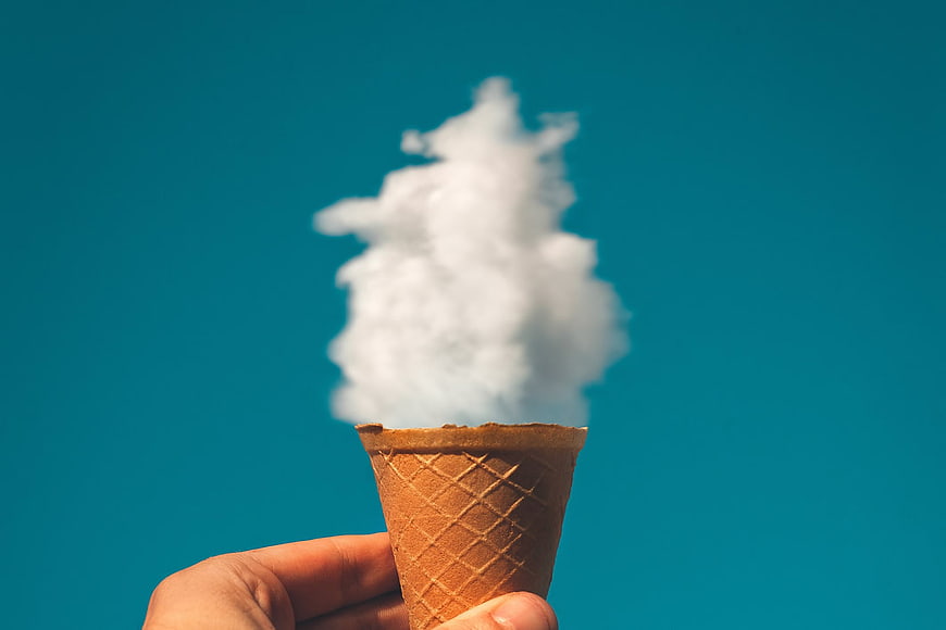 Hand Holding Ice Cream Cone with Cloud Against Blue Sky