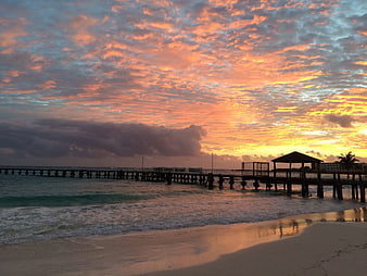 Dramatic sunset over tropical pier with vibrant orange clouds