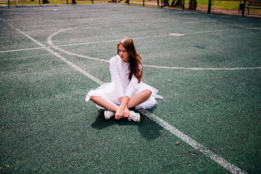 Young woman in white dress sitting on tennis court