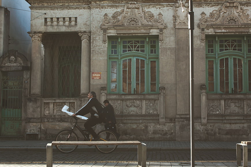 Man riding bicycle past historic building facade